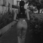 Monochrome photo capturing a woman walking outdoors on a pathway lined with plants.
